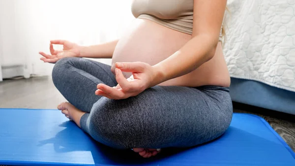Donna incinta con grande pancia meditatng mentre seduto in posa loto sul tappeto fitness a casa. Concetto di stile di vita sano, assistenza sanitaria e sport durante la gravidanza — Foto Stock