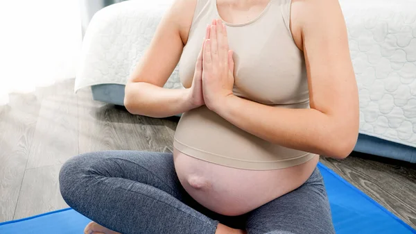 Primo piano della donna incinta che medita e si rilassa sul tappeto fitness a casa. Concetto di stile di vita sano, assistenza sanitaria e sport durante la gravidanza — Foto Stock