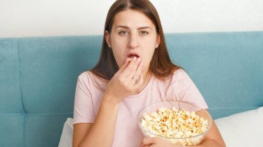 Hafta sonları pijama giyen, yatakta televizyon izleyen ve büyük kaseden patlamış mısır yiyen genç bir kadının portresi.