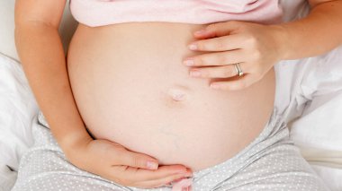 Müstakbel annenin eli yavaşça karnına dokunuyor. Ebeveynlik kavramı ve gelecekteki bebeğin mutlu beklentisi.