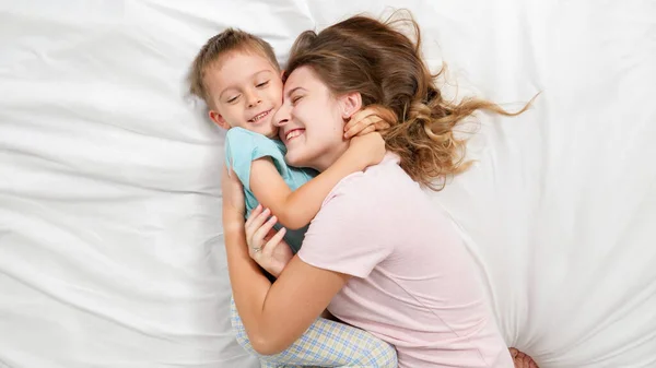 Widok z góry portret cute little boy leżącego z młodą matką na łóżku i rozmowy. Pojęcie rodzicielstwa i szczęścia rodzinnego — Zdjęcie stockowe
