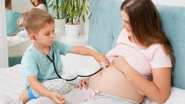 Doktorda oynayan sevimli çocuk ve steteskopla hamile annenin kalp atışlarını dinliyor. Hamilelik süresince sağlık ve tıbbi muayene kavramı — Stok fotoğraf