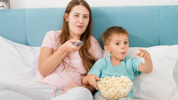 Genç annesiyle birlikte televizyonda film izleyip patlamış mısır yiyen mutlu bir çocuk.