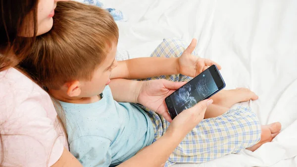 Young pregnant mother showing ultrasound image of her baby to older son. Concept of healthcare and family happiness expecting baby — Stock Photo, Image