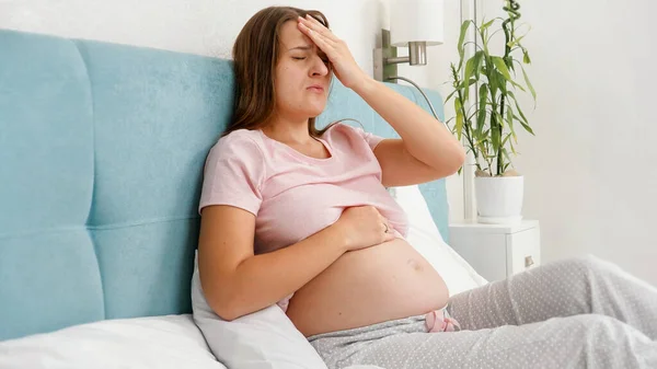 Mujer embarazada joven en pijama sintiendo dolor de cabeza tocando su cabeza. Concepto de salud y dolor durante el embarazo —  Fotos de Stock
