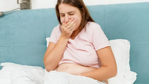 Porträtt av en sjuk gravid kvinna som känner sig illamående och hostar när hon ligger i sängen på morgonen. Sjukvård och förgiftning under graviditet — Stockfoto