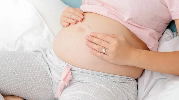 Draufsicht einer schwangeren Frau im Schlafanzug, die ihren dicken Bauch umklammert und berührt. Konzept der Elternschaft und der glücklichen Erwartung eines zukünftigen Babys. — Stockfoto