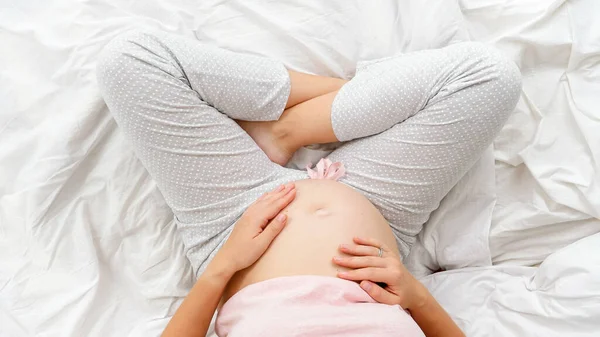 Närbild av ganska gravid ung kvinna röra och smeka hennes ofödda barn i stor mage. Vacker graviditet och förväntan på barnet — Stockfoto