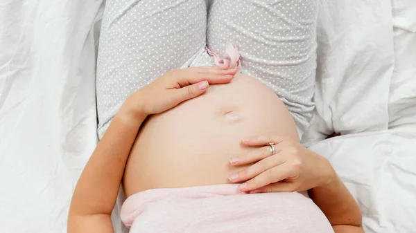 Visão superior da jovem grávida descansando na cama suavemente acariciando e tocando sua barriga. Bela gravidez e antecipação do bebê — Fotografia de Stock
