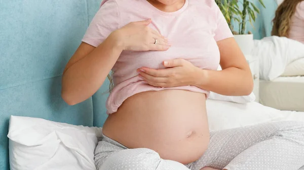 Молодая беременная женщина с большим животом проверяет и трогает грудь перед лактацией. Концепция охраны беременности и медицинского обследования — стоковое фото