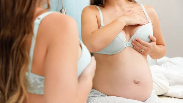 Красивая беременная женщина в бюстгальтере с большим животом, сидящая перед зеркалом и глядя в отражение на животе. Красивая беременность и ожидание ребенка. — стоковое фото