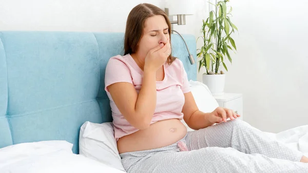 Ung gravid kvinna mår illa vilar i sängen och hosta i handen. Begreppet graviditetshälsa och läkarundersökning. — Stockfoto