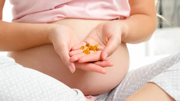 Fechar-se de pílulas de vitamina na mão da mulher grávida no pijama. Conceito de cuidados de saúde de gravidez e suprimentos médicos femininos — Fotografia de Stock