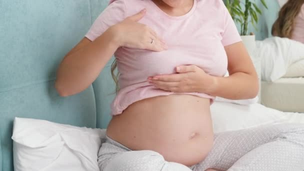Junge schwangere Frau mit dickem Bauch, die ihre Brust vor der Stillzeit kontrolliert und berührt. Konzept der Schwangerschaftsvorsorge und der medizinischen Untersuchung — Stockvideo