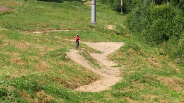 Joven montando en bicicleta de montaña por la empinada colina y saltando en trampolines — Vídeo de stock