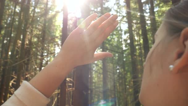 Beautiful young woman looking on bright sun through her fingers while relaxing in pine forest at mountains — Stock Video