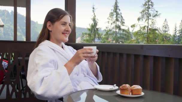 Portret szczęśliwej uśmiechniętej kobiety relaksującej się na balkonie hotelowym i cieszącej się śniadaniem rano. Pojęcie osób podróżujących, turystyki i wakacji w górach w lecie — Wideo stockowe
