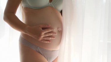 İç çamaşırlı güzel hamile kadın büyük pencerede dikilip dışarı bakıyor. Mutlu hamilelik ve bebek beklentisi kavramı