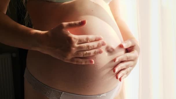 Detailní záběr těhotné ženy stojící na slunci a jemně hladící její velké břicho. Koncept šťastného těhotenství a očekávání dítěte — Stock video