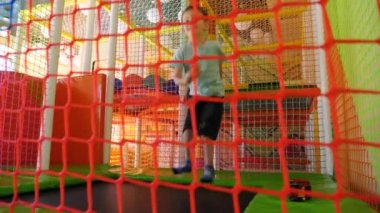 İçerideki çocuk bahçesinde trambolinde zıplayan ve oynayan neşeli küçük çocuğun güvenlik ağından bakın.