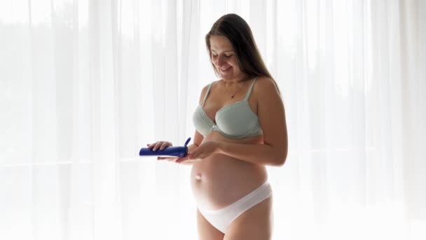 Feliz sorrindo mulher grávida esperando um bebê aplicando creme hidratante ou loção em sua pele corporal. Conceito de beleza, gravidez e cuidados de saúde. — Vídeo de Stock