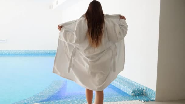 Вид спереду молода красива жінка в купальнику знімає халат перед прогулянкою в басейні на готельному курорті — стокове відео