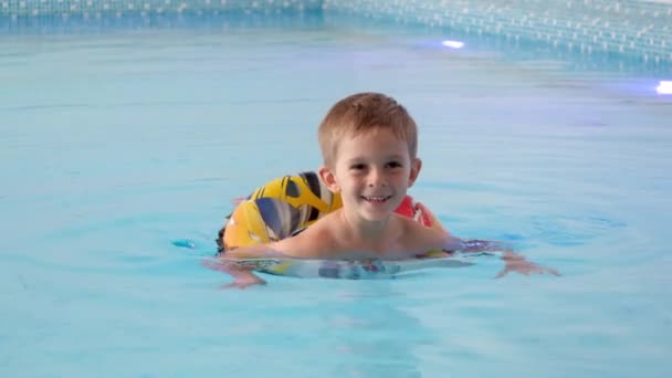 Happy uśmiechnięty mały chłopiec pływanie w krytym basenie. — Wideo stockowe