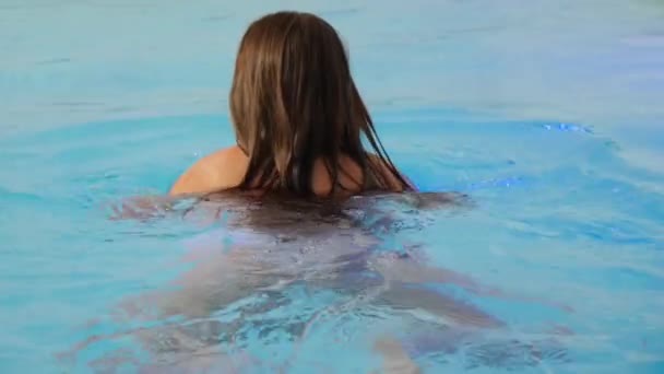 Vista trasera de la joven morena nadando y relajándose en la piscina cubierta en el spa en el complejo hotelero — Vídeo de stock