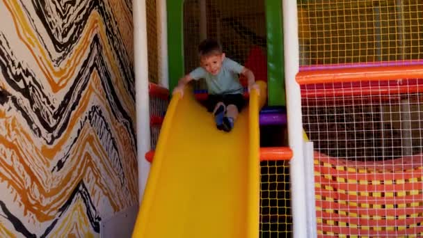 Felice ridendo ragazzino cavalcando lo scivolo sui bambini palyground e immersioni in piscina con palline di plastica colorate. — Video Stock