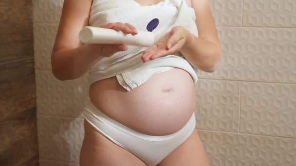 Gros plan de la femme enceinte appliquant crème hydratante sur la peau du corps après avoir pris une douche dans la salle de bain. Concept de beauté féminine, soins du corps et soins de santé pendant la grossesse. — Video