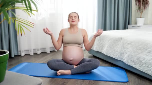 Hermosa mujer embarazada sonriente sentada en loto asana y meditando. Concepto de salud y deportes durante el embarazo — Vídeo de stock