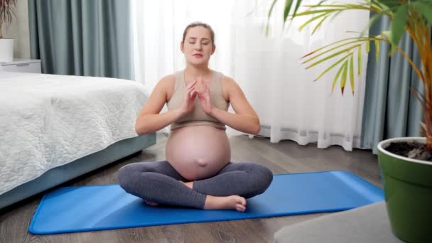 Bela mulher grávida sorridente praticando ioga sentado na aptidão louco em pose de lótus e respirar profundamente. Conceito de cuidados de saúde e esportes durante a gravidez — Vídeo de Stock