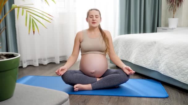 Bella donna incinta meditando e praticando yoga sul tappeto fitness a grande finestra a casa. Concetto di stile di vita sano, assistenza sanitaria e sport durante la gravidanza — Video Stock