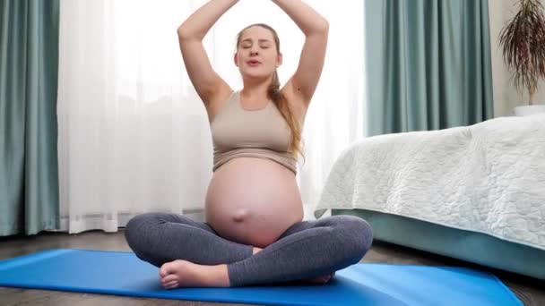 Красива вагітна жінка робить вправи для йоги і дивиться на її великий живіт. Концепція здорового способу життя, охорони здоров'я та спорту під час вагітності — стокове відео