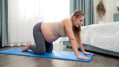 Güzel hamile bir kadın yatak odasındaki spor paspası üzerinde yoga egzersizleri yapıyor. Hamilelik boyunca sağlıklı yaşam tarzı, sağlık ve spor kavramı