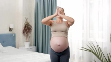 Neşeli, gülümseyen, yoga yapan ve güneşli bir sabahta büyük pencerenin yanında derin nefes alan hamile kadın. Hamilelik boyunca sağlıklı yaşam tarzı, sağlık ve spor kavramı