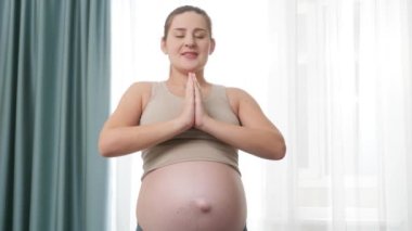 Senin portren, yoga yaparken ellerini katlayan ve derin derin nefes alan hamile bir kadın. Hamilelik boyunca sağlıklı yaşam tarzı, sağlık ve spor kavramı