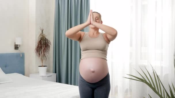 Glad leende gravid kvinna utövar yoga och andas djupt intill stora fönster på solig morgon. Begreppet hälsosam livsstil, hälsovård och idrott under graviditeten — Stockvideo