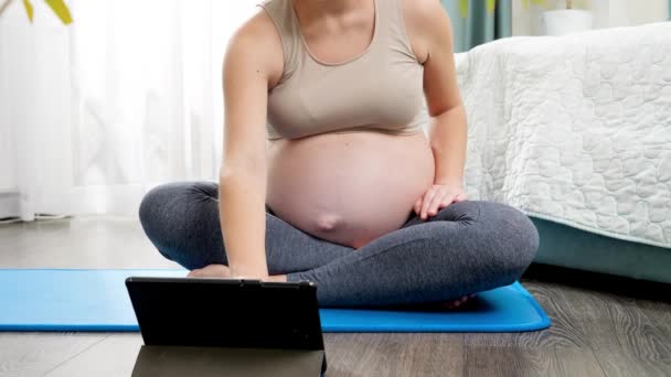 Hamile bir kadının internetten yoga dersi izlemesi ve evdeki spor paspası üzerinde meditasyon yapması. Hamilelik boyunca sağlıklı yaşam tarzı, sağlık ve spor kavramı — Stok video