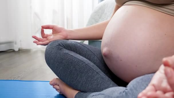 Jonge zwangere vrouw ademt diep en zit in lotushouding terwijl ze thuis yoga-oefeningen doet. Concept van gezonde levensstijl, gezondheidszorg en sport tijdens de zwangerschap — Stockvideo