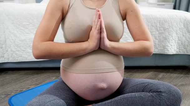 Zbliżenie młodej medytującej kobiety w ciąży siedzącej na macie fitness w sypialni z dużym oknem. Pojęcie zdrowego trybu życia, opieki zdrowotnej i sportu w czasie ciąży — Wideo stockowe