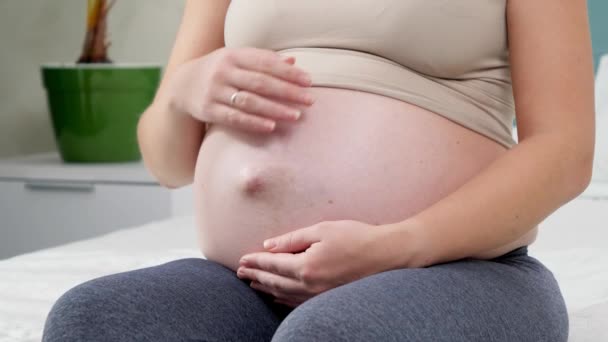 Primer plano de la joven embarazada con ropa deportiva sentada en la cama y acariciando suavemente su vientre. Concepto de estilo de vida saludable, atención médica y deportes durante el embarazo — Vídeo de stock