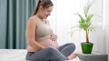 Genç hamile kadın yatakta dinleniyor ve koca göbeğini okşuyor. Hamilelik boyunca sağlıklı yaşam tarzı, sağlık ve spor kavramı