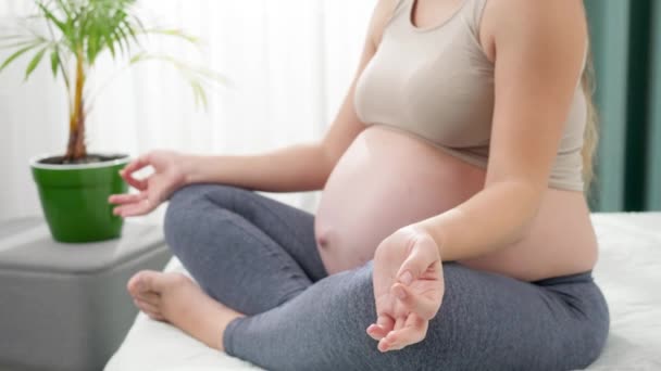 Lachende zwangere vrouw in legging en fitness top mediteren op bed in de ochtend. Concept van gezonde levensstijl, gezondheidszorg en sport tijdens de zwangerschap — Stockvideo