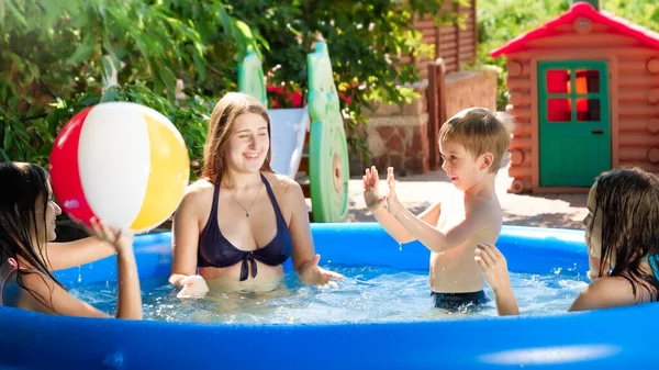 Cheerful bog family playing with beach ball in inflatable swimming pool in the backyard garden. Family summer vacation and holidays — Stock Photo, Image