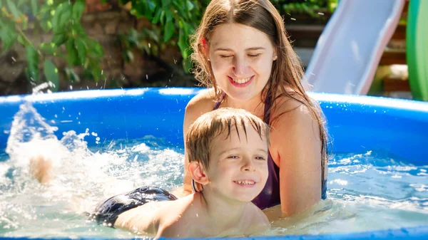 Happy smiling mother teaching swimming her little son in swimming pool at house backyard garden. Family summer vacation and holidays — Stock Photo, Image