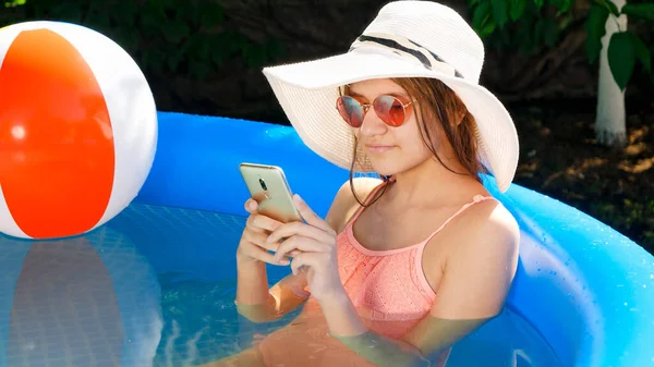 Retrato de una hermosa chica joven relajándose en la piscina al aire libre en el patio trasero y escribiendo mensaje en el teléfono inteligente. Concepto de felices vacaciones de verano y vacaciones — Foto de Stock