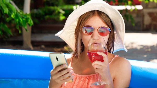 Mooi glimlachend meisje drinken cocktail en het gebruik van smartphone terwijl ontspannen in opblaasbaar zwembad — Stockfoto