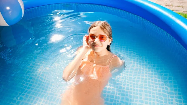 Top view of happy smiling girl in sunglasses lying and relaxing in utdoor swimming pool. Concept of happy and cheerful summer holidays and vacation — Stock Photo, Image