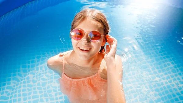 Retrato de una hermosa adolescente sonriente en gafas de sol y bañador relajándose en la piscina al aire libre. Concepto de felices y alegres vacaciones de verano y vacaciones —  Fotos de Stock